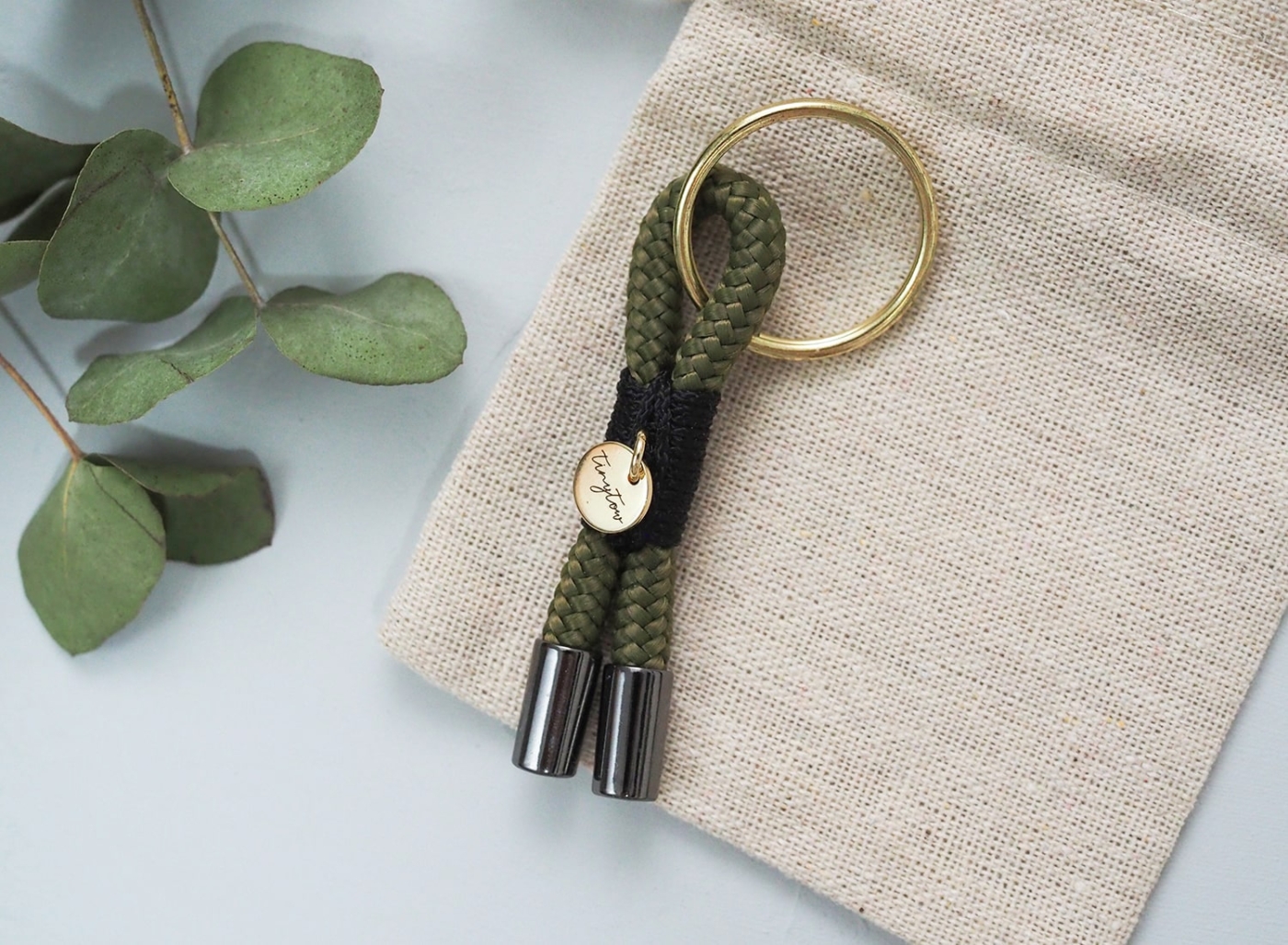 Kleiner Schlüsselanhänger aus grünem Tau mit schwarzen und goldenen Elementen.
