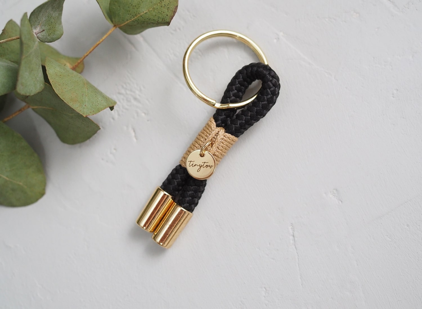 Schlüsselanhänger aus schwarzem Tauseil mit beigefarbenen Details und goldenem Schlüsselring.